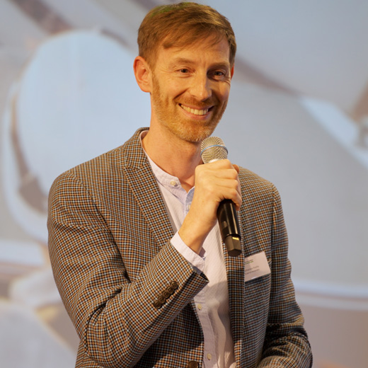 Mann steht vor einer Leinwand und spricht bei einem Vortrag in ein Mikro